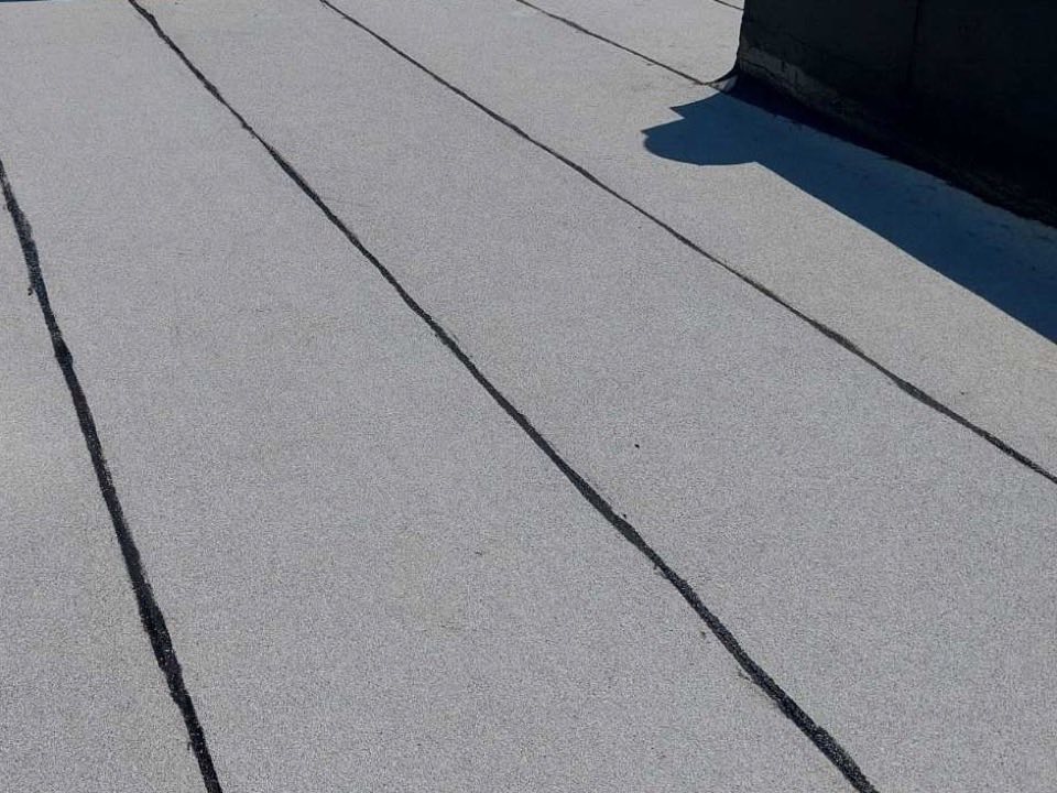 Close-up of a granulated modified bitumen membrane on a flat roof, with sealed seams running to a parapet wall
